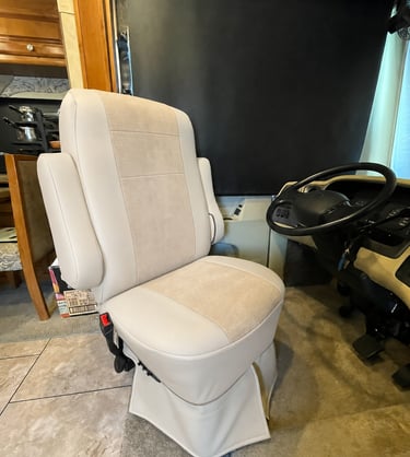 A plush tan leather swiveling captain chair in a luxury RV driver cabin with a black steering wheel.