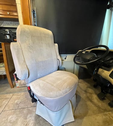 Beige fabric swivel driver's seat inside a motorhome RV cockpit next to the steering wheel.