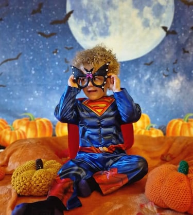 Young curly haired boy dressed as superman with a night backdrop for halloween special class.