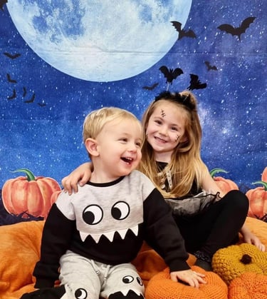 2 children, brother and sister dressed up for halloween sat surrounded by pumpkins