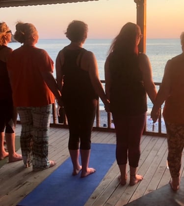 A group of women holding hands and looking out to sunset over the sea
