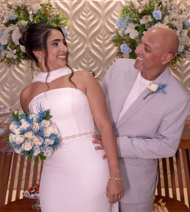 Noivos sorridentes posando com flores de casamento azuis e brancas em um local de recepção formal.