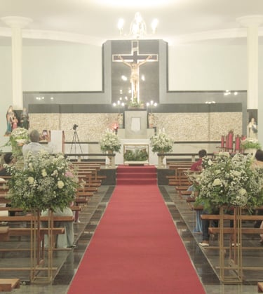 Cerimônia de casamento em uma igreja com tapete vermelho no corredor, arranjos de flores brancas e c