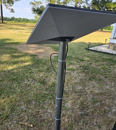 A Starlink satellite internet dish mounted on a metal pole in a grassy backyard.