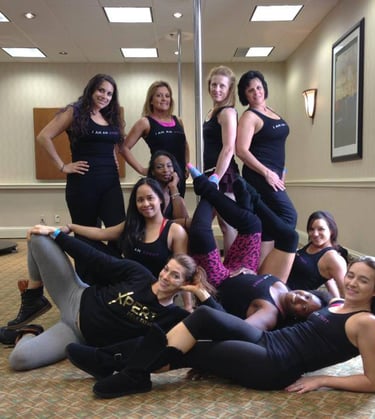 Photo of 10 people wearing black tank tops posing around a stage pole in a hotel conference room