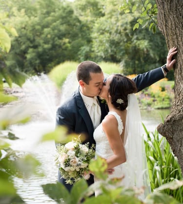 a bride and groom kissing in front of a pond