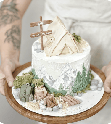 a person holding a cake with a mountain scene