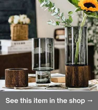 Layered minimalist glass vases with dark wood bases styled with a single sunflower on a bright table