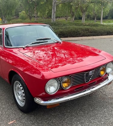A photo of a red 1974 Alfa Romeo GTV 2000 in a park setting.