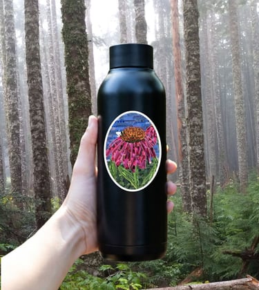 Hand holding a black reusable water bottle with a flower sticker in a foggy evergreen forest.