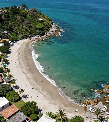 An aerial drone perspective of a pristine turquoise bay in Puerto Escondido, Oaxaca. The scene showcases the natural beauty and the exclusive lifestyle offered by premium real estate developments in the region.