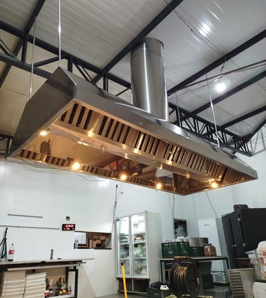 Stainless steel commercial kitchen exhaust hood with lights installed over a food preparation area.