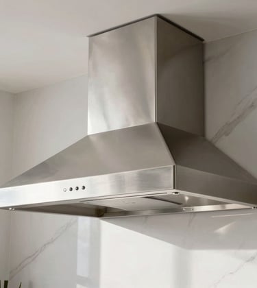 A minimalist close-up of a custom residential stainless steel hood in a bright, modern São Paulo kitchen. The brushed metal finish catches the morning light. Background shows white marble and clean architectural lines. Luxury South American home.