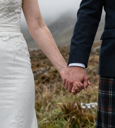 A close-up photograph of a Northern European / Scottish bride and groom holding hands during an elopement ceremony in a wild, misty glen.