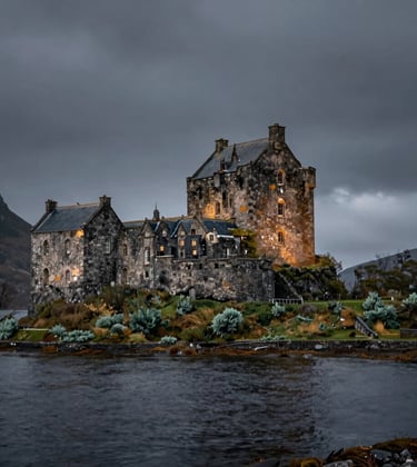 A high-end, cinematic photograph of a historic stone castle on the edge of a dark loch in the Northern European / Scottish Highlands. The architecture is illuminated by soft, moody light against a deep slate grey sky, surrounded by muted sage green foliage.