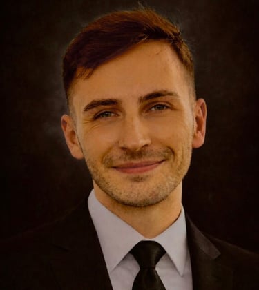 A smiling Bradley in a black suit and tie against a dark background.