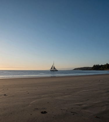 A wide-angle, cinematic photograph of a tranquil North American / Coastal inlet at dusk. The sky is a blend of sand and deep blue, with the silhouette of a lone sailing boat in the distance, conveying a sense of timeless travel and lived experience.