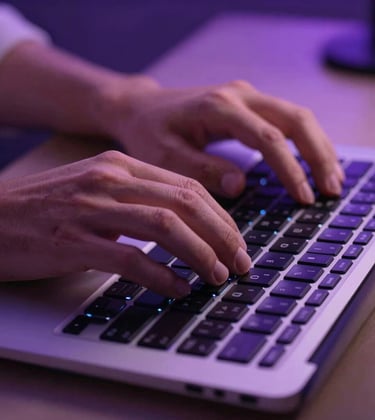 Close-up photography of a professional's hands typing on a high-end backlit keyboard in a North American / Global Professional environment. Soft purple ambient light and a clean aesthetic.