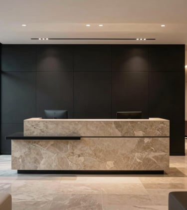 A high-end South Asian / Indian commercial office reception area. Matte black paneling contrasts with warm taupe stone accents. Minimalist furniture and a large, clean-lined reception desk define the space. The lighting is focused and professional, highlighting premium craftsmanship and detail.