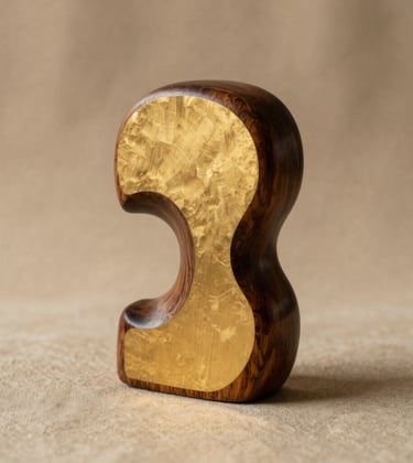 A professional studio photograph of a handcrafted wooden sculpture with a matte gold inlay. The object sits on a warm beige linen cloth. The lighting is soft and directional, creating gentle shadows that emphasize its organic curves.