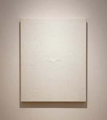 Minimalist photography of an abstract realist painting with heavy texture and soft white highlights, centered on a warm ivory wall.