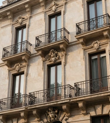 Architectural detail of a historic luxury apartment building in Milan. Elegant wrought iron balconies, cream-colored stone facade, and large ornate windows. Soft morning sunlight. European High-Net-Worth setting.