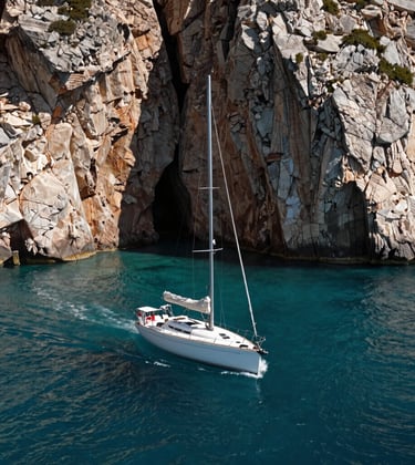 Photography of a private sailboat navigating between high rocky cliffs in a hidden Iberian cove, deep teal water, sophisticated composition, bright sunlight.