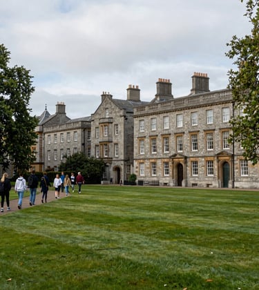 A wide-angle shot of a lush green university campus in Dublin, Ireland, featuring historic stone buildings and a group of students walking along a path. The atmosphere is academic and serene. North American / US photography style.