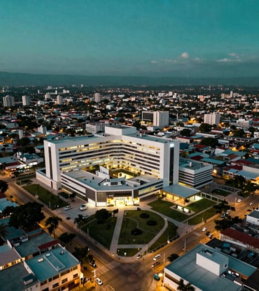 A drone shot showing the proximity of new luxury developments to major hospital zones in Mérida, North American / Mexican (Yucatán). The city looks vibrant and modern under a Deep Sea Green twilight sky.