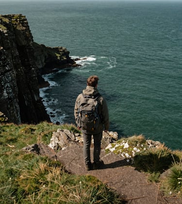 a man wearing a backpack who is looking at the sea from the coastal path