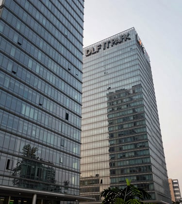 A grand architectural view of the DLF IT Park glass buildings in Chennai, reflecting a soft off-white sky, highlighting the commercial proximity.
