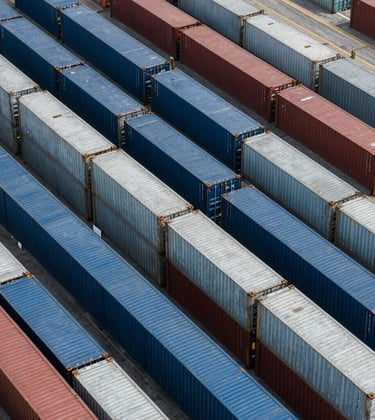 An aerial view of the modern container terminal showing organized rows of shipping containers in shades of muted steel blue and silver blue.