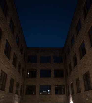 An architectural photograph looking up a dark, narrow courtyard towards a square of night sky in an international business capital. Minimalist, quiet, and authoritative.
