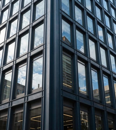 Professional photography of a modern commercial office building exterior in a US downtown area, with clean architectural lines and bright daylight reflecting off charcoal blue steel elements.