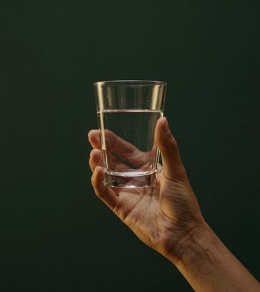 Minimalist shot of an elegant person's hands holding a glass of water, lit by soft golden light. Deep green background, cinematic South American setting, serene and powerful.