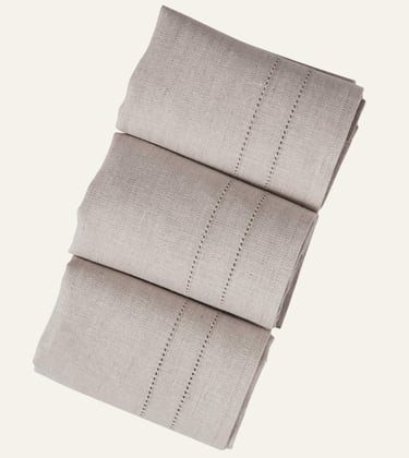 Three folded beige linen napkins with elegant hemstitch detailing for a neutral table setting.