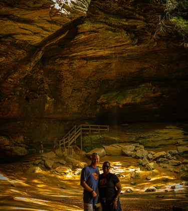 A couple and their dog posing in front of a massive rock cave and waterfall at Hocking Hills State Park.