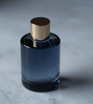 A minimalist, dark glass perfume bottle resting on a cold marble surface. Soft gold highlights (#B08D5B) on the cap, shadows in deep blue (#0C1E38), atmospheric lighting.