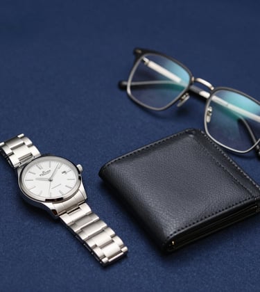 Detailed shot of premium men's accessories: a silver watch, a slim leather wallet, and luxury eyewear placed on a clean navy fabric background. Sharp lines, sophisticated metallic glints, understated power.