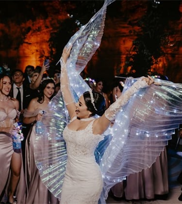 Novia muy contenta bailando con velo iluminado por luces led el día de boda, atrás de ella sus damas
