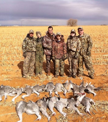 Four hunters in camouflage posing with their limit of Sandhill Cranes after a successful Texas Panhandle hunt.