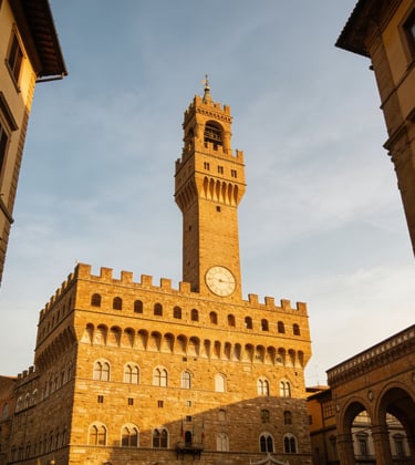 The historic Palazzo Vecchio tower in Florence, Italy, glowing in golden sunset light against a blue sky.