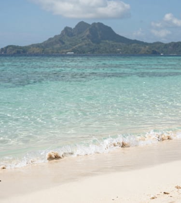 A scenic view of Gili Terawangan beach with crystal clear water and a distant view of Lombok's mountains. Tropical vibes, clean and bright lighting, incorporating #78909C tones in the water and #FDF6ED in the sand.