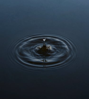 A professional fine-art photograph of a single ripple Expanding across a dark earthy blue pool of water. The composition is minimalist and centered, capturing perfect stillness interrupted by a moment of presence.