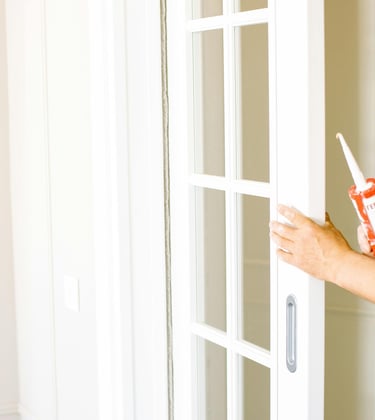 A person caulking a door frame as a way of keeping out drafts and lowering utility bills.