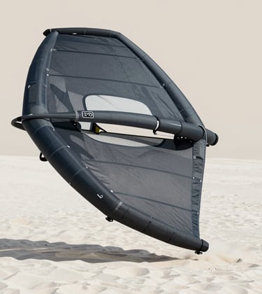 A close-up of a high-performance kitesurfing wing resting on white sand. The texture of the fabric is visible. Minimalist composition with a focus on lines and gear. Colors include the deep charcoal of #2C3539 against the sand's #FAF8F5.