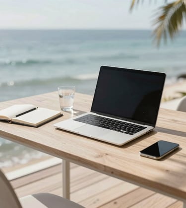 An overhead shot of a minimalist workstation on a wooden deck by the ocean. A high-end laptop, a notebook, and a glass of water. The scene is bathed in natural, bright light with soft shadows of palm fronds, using #FAF8F5 and #7E8A7F tones.