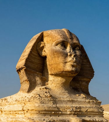 A symmetrical close-up photograph of the Great Sphinx of Giza. The stone is illuminated by the morning sun, casting warm gilded gold tones against the deep Egyptian blue of the sky.