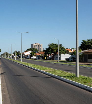 Clean, professional photography of modern street infrastructure in a Brazilian allotment, featuring high-quality asphalt, green medians, and sophisticated lighting poles against a clear blue sky.