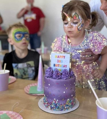 Young girl leaning over a birthday cake, unicorn painted on her face